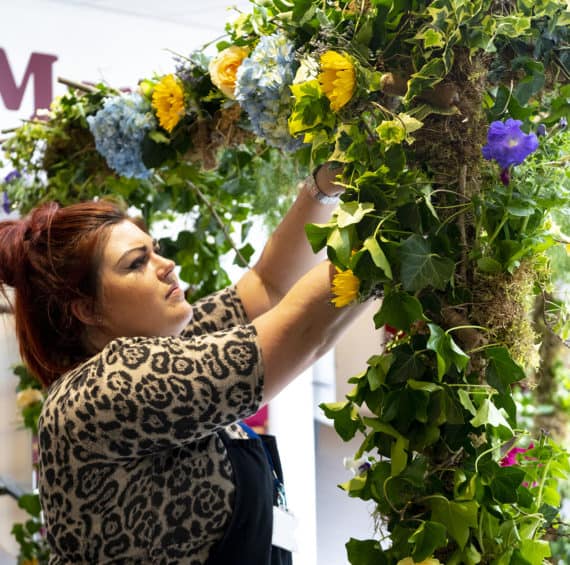 Woman arranging colourful flowers on a floral display at Capel Manor College.