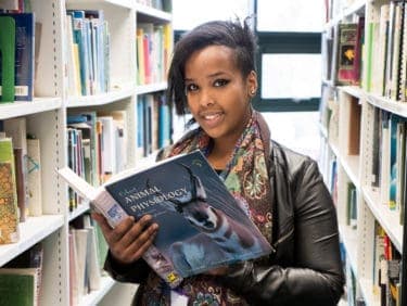 Female student in the library at Capel Manor College, reading an animal physiology book.