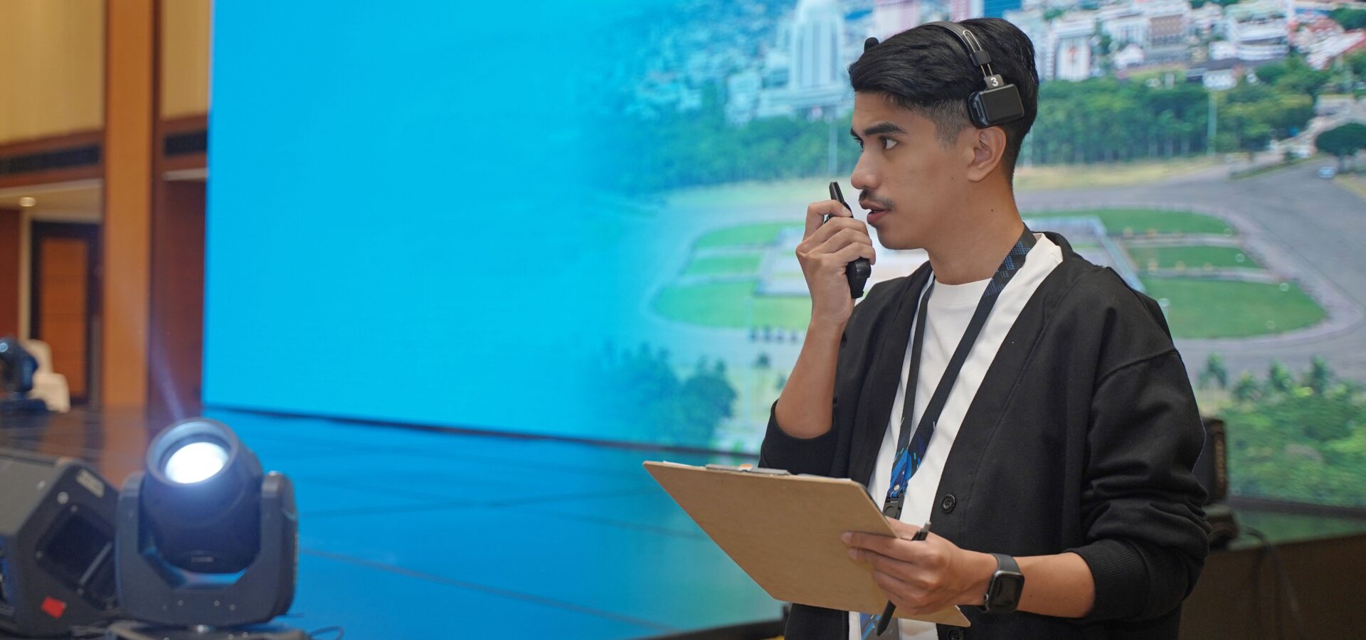 Student running an event - holding a walkie talkie with a stage behind them.