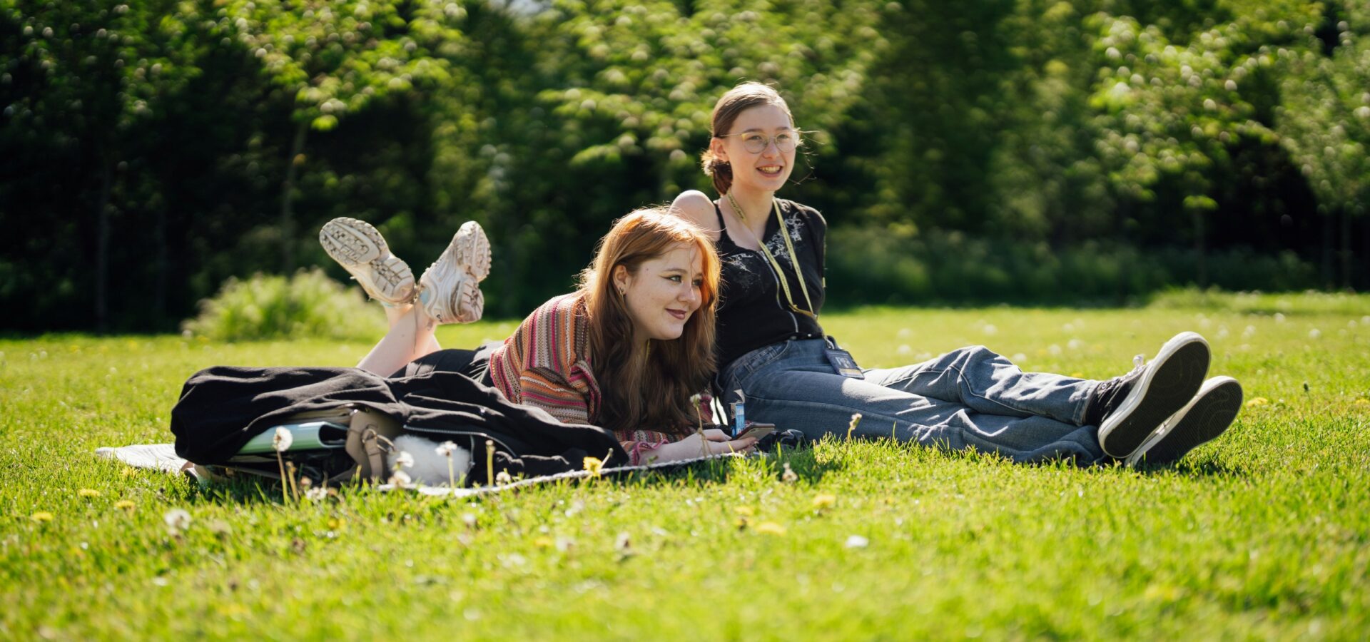 Two students sitting on the grass and enjoying the sunshine at Capel Manor College's Enfield Campus.