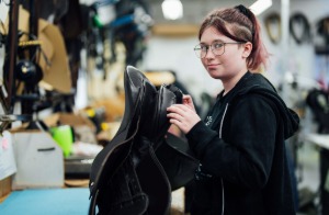 A saddlery student at Capel Manor College holding a saddle that they have designed and created by hand.